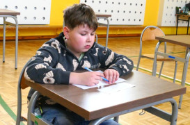 Chłopiec siedzący przy stoliku. Chłopiec w ręku trzyma długopis 
