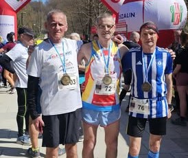 Trzej panowie w strojach sportowych stoją obok siebie 