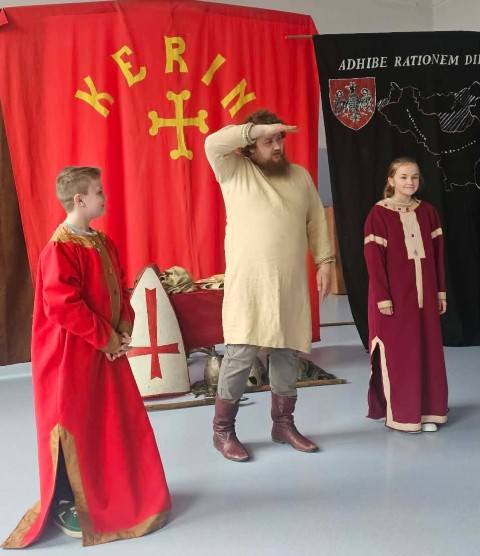 Mężczyzna i dwoje dzieci stoją obok siebie. Wszyscy ubrani są w stroje historyczne