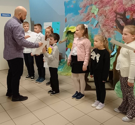 Dzieci stoją w szeregu. Mężczyzna wręcza im dyplomy 