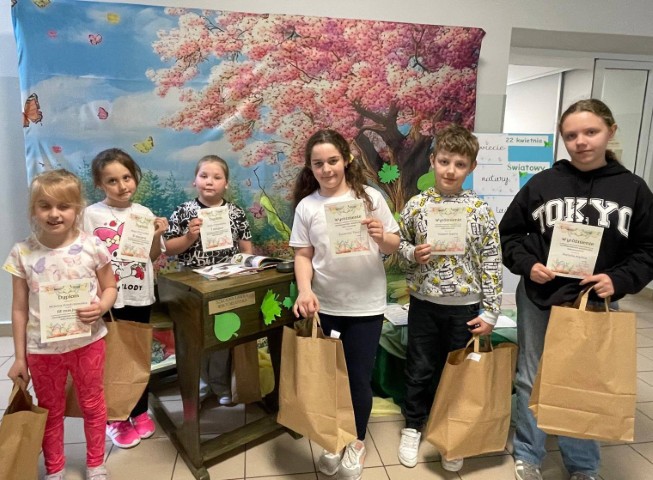 Grupa dzieci: dziewczynki i chłopcy stoją obok siebie. Dzieci trzymają w dłoniach dyplomy 