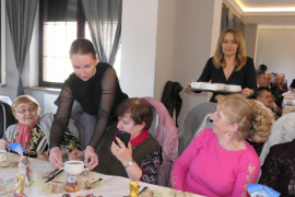 Kobiety rozdają potrawy osobom siedzącym za stołem 