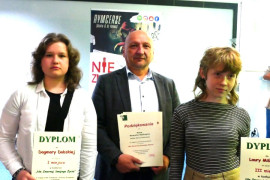 Laureatki konkursu trzymają w ręku dyplomy. Towarzyszy im mężczyzna, który również trzyma w ręku dyplom  
