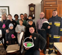 Grupa osób: dorośli i dzieci stoją obok siebie. Osoby znajdują się w pokoju 