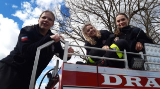 Trzy młode kobiety siedzą na dachu strażackiego wozu bojowego