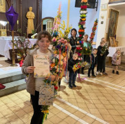 Dziewczynka trzyma w ręku dyplom. Widoczne są palmy