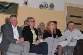 Osoby siedzą na krzesłach i oglądają występ zespołu muzycznego