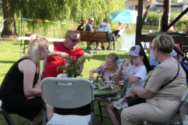 Dorośli i dzieci siedzą przy stole. Trwa rodzinny piknik 
