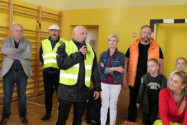 Osoby stoją obok siebie. Mężczyzna trzyma w ręku mikrofon. 