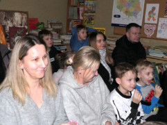 Grupa osób: dorośli i dzieci siedzą obok siebie na krzesłach 
