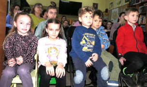 Grupa dzieci. Dzieciaki siedzą obok siebie na krzesłach 