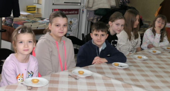 Sześcioro dzieci: dziewczynki i chłopiec siedzą obok siebie przy stole