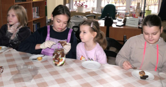 Cztery dziewczynki siedzą przy stole. Dziewczynki przygotowują słodkie babeczki