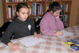 Dwie dziewczynki siedzą obok siebie przy stole. Przed dziewczynkami leżą białe kartki papieru 