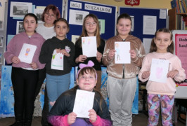 Sześć dziewczynek i kobieta stoi obok siebie. Dziewczynki trzymają w ręku wykonane przez siebie rysunki