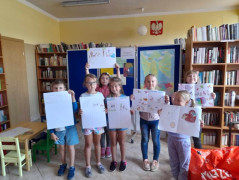 Grupa dzieci trzymająca w rękach kartki papieru, na których znajdują się wykonane przez nich rysunki