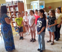 Grupa dzieci i kobieta. Spotkanie z pisarką w bibliotece 