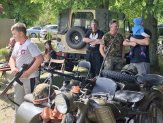Dorośli i chłopiec. Stoisko wystawiennicze, na którym znajdują się repliki broni. Chłopiec trzyma w dłoni replikę karabinu 