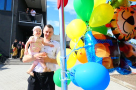 Mężczyzna trzyma na ręku małe dziecko. Obok powiewają balony