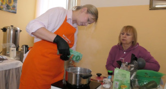 Dwie kobiety. Jedna z nich wrzuca makaron do garnka, w którym gotuje się woda 