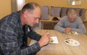 Dwaj panowie siedzą przy stole. Panowie spożywają posiłek. Uczestnicy warsztatów kulinarnych 