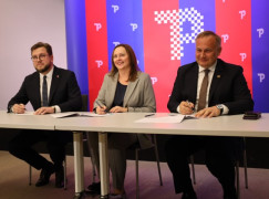 Trzy osoby siedzące za stołem. Moment podpisania porozumienia 