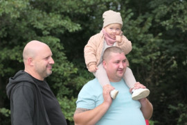 Dwaj mężczyźni stoją obok siebie. Na barkach jednego z nich siedzi mała dziewczynka