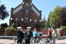Grupa osób z rowerami stoi przed kościołem w Dziepółci 