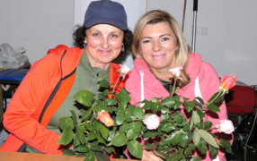 Dwie kobiety siedzące obok siebie. Kobiety trzymają w dłoniach bukiety róż 