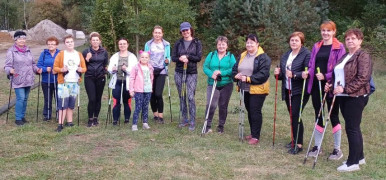 Grupa osób - uczestniczki marszu Nordic Walking stoją obok siebie. Każda z nich ubrana jest w sportowy strój oraz trzyma w ręku kije NW