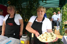 Dwie panie stoją obok siebie. Jedna z nich trzyma talerz, na którym znajdują się pierogi 