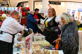 Trzy panie przy stoisku wystawienniczym. Jedna z pań kroi ciasto 
