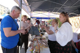 Stoisko wystawiennicze, na którym znajdują się m.in ciasta. Widać osoby sprzedające i kupujące 