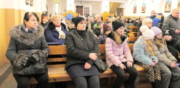 Osoby siedzą w kościelnych ławkach 