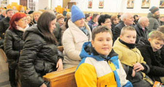 Dorośli i dzieci siedzą w kościelnych ławkach