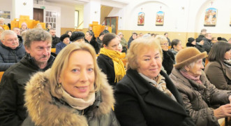 Grupa osób siedząca w kościelnych ławkach 
