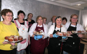 Grupa kobiet stoi obok siebie. Kobiety trzymają na tacach pączki
