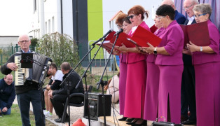 Chór podczas występu scenicznego. Widoczny mężczyzna grający na akordeonie 