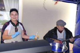 Kobieta i mężczyzna. Kobieta obsługuje grill, a mężczyzna gra na instrumencie 