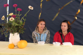 Dwie kobiety siedzące za stołem, na którym znajduje się kompozycja kwiatowa 