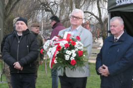 Trzech mężczyzn stoi obok siebie. Jeden z nich trzyma wiązankę kwiatów