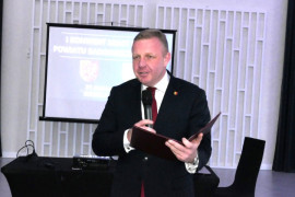 Mężczyzna podczas przemówienia. Mężczyzna trzyma w ręku mikrofon i dokumenty