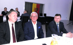 Trzej mężczyźni siedzą obok siebie przy stole 