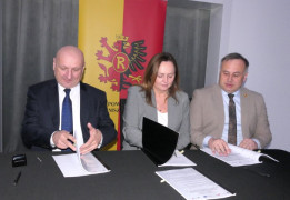 Trzy osoby siedzą za stołem moment podpisywania umowy