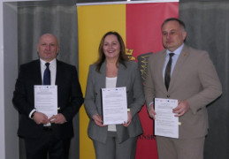 Trzy osoby stoją obok siebie. Dwaj mężczyźni i kobieta trzymają w ręku dokumenty
