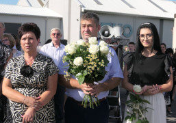 Grupa osób stojąca obok siebie. Mężczyzna trzyma bukiet białych róż