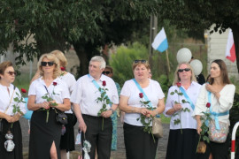 Grupa osób. Kobiety trzymają białe róże 