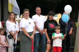 Grupa osób stojąca obok siebie. Chłopiec trzyma biało-niebieskie balony 