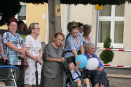 Grupa osób. Dziecko siedzące w wózku trzyma balony