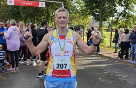 Mężczyzna w stroju sportowym. W geście zadowolenia ma dłonie uniesione do góry 